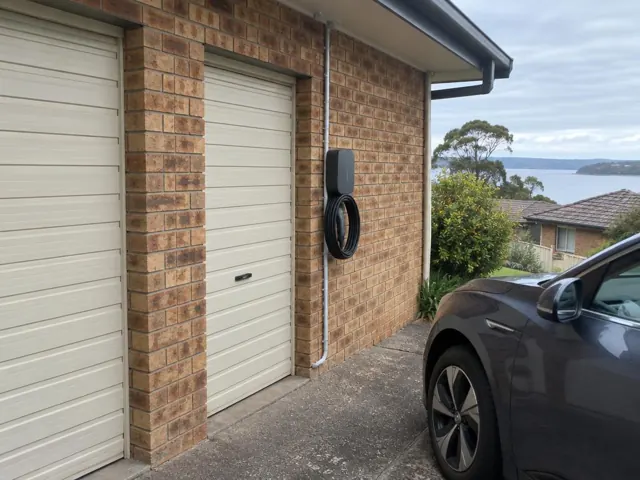 Wall-mounted EV charger with coiled cable on a brick garage wall beside a driveway in Kilaben Bay